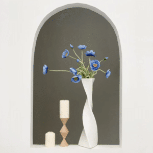Grand vase blanc en forme de torsade posé sur rebord contenant des fleurs bleues