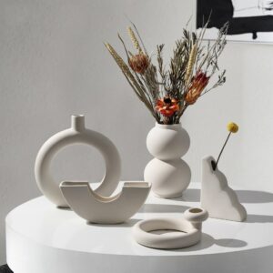 Collection de petits vases en céramique blanche de style scandinave à formes géométrique variées et originales dans un décor minimaliste avec un bouquet de fleurs à pampa sur une table ronde.