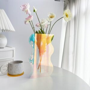 Vase transparent de forme géométrique ondulée, il a des reflets multicolores et contient un mélange de fleurs blanches.