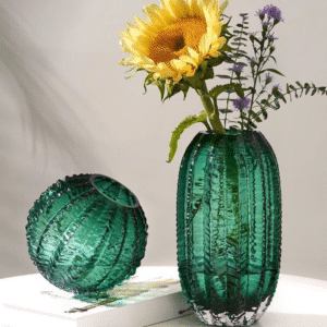 Ce vase art déco en verre à la forme d'un cactus. Disponible en forme ronde ou ovale, sa surface est parsemée de petites aspérités qui rappellent les aiguilles d'un cactus. Sa couleur verte se confond également avec celle de la plante.