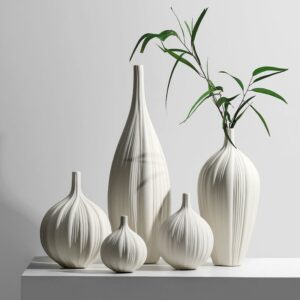 Des vases blancs en céramique de différentes formes arrondies. Il y a cinq vases sur la photos, positionnées sur un meuble blanc, avec un mur blanc en arrière plan. Les vases sont striés, comme le revêtement d'un végétal. Cela donne l'impression d'une écorce de citrouille. Ces vases soliflores sont modernes. L'un d'eux contient une branche de bambou.