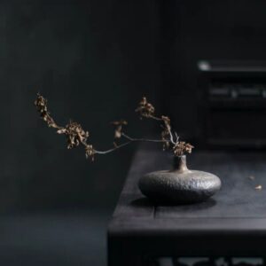 Vase chinois plat en forme de disque, assimilé au rituel du thé en Chine. Le vase est dans les tons bruns, avec des reflets bronze. Sa surface est faite d'aspérités. Il est composé de porcelaine et de céramique.