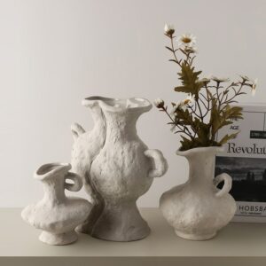Vase grec blanc en terre cuite fabriqué à la main. Son style est brut, simple, comme fabriqué à partir de boue, dans des courbes approximatives. Il contient des fleurs séchées ressemblant à des chardons et des pissenlits.