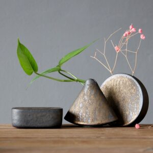 Vase japonais miniature en forme ronde ou triangulaire. Il est fabriqué à la main, en céramique. C'est un soliflore de couleur métal avec des reflets bronze. Il contient une branche de petite fleur.