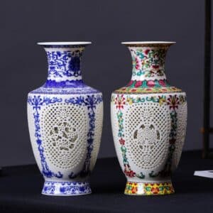 Deux vases en porcelaine de style chinois antique. Un bleu et blanc, et l'autre de plusieurs couleurs, blanc, rose, vert et jaune. Ils sont ornés de motifs floraux traditionnels. Ils sont perforés au centre par une multitude de petits trous formant un motif géométrique. Les vases sont en forme de jarre typique du style chinois. Les deux vases sont posés à même le sol sur un revêtement noir.
