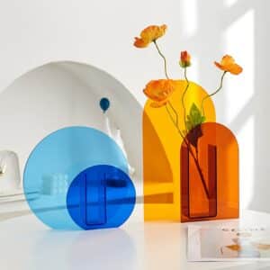 Vase scandinave à forme géométrique coloré. On voit un vase bleu rond ainsi qu'un autre vase ovale de couleur orange. Ces vases sont fabriqués en acrylique pour un aspect transparent et fin qui ravira vos fleurs préférées.