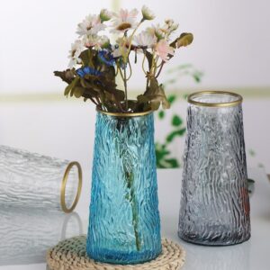 Vases en verre de forme tubulaire évasé, de couleur bleu, gris et transparent. Le verre est strié sur toute la surface. Un anneau doré est inséré au niveau de la bouche du vase. Le vase bleu contient un petit bouquet de fleurs séchées.
