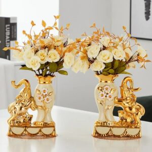 Vase vintage en céramique à l'effigie d'un éléphant. Le vase est doré et brillant. Il scintille de mille feux grâce à ses dorures, brillants et paillettes. Deux vases sont exposés sur une table blanche, contenant chacun un bouquet de rose blanche.