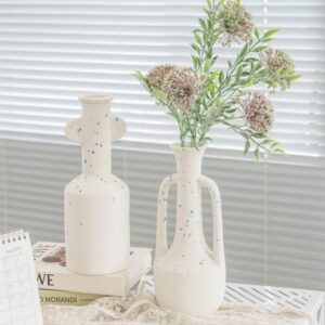 Vase grec en blanc en forme de jarre avec deux anses. Un des vases contient un bouquet de fleurs séchées. Le vase est tacheté de gouttes bleues ce qui apporte un aspect moderne et une nouvelle interprétation du vase grec.