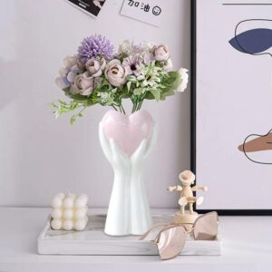 Vase blanc en forme de cœur tenu par des mains en céramique blanche et rose. Ce joli vase diffuse un style romantique dans votre décoration d'intérieur. À la fois subtil et original, il permet de valoriser vos plus jolis bouquets de fleurs.