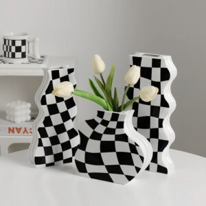Vase art déco en forme géométrique abstraite quadrillé en noir et blanc. Ce vase est disponible en trois tailles différentes. Le plus petit modèle contient un bouquet de tulipes blanches. Les vases sont exposés sur une table blanche.