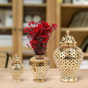 Vase céramique en forme de petite jarre dorée. Ce vase est exposé en trois formats. Le vase central contient un bouquet de fleurs rouge. Ce vase à l'apparence d'un petit pot et il est doté d'un couvercle. De plus, sa surface percée lui permet d'offrir un jeu de transparence unique.