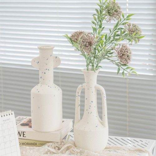 Vase grec en blanc en forme de jarre avec deux anses. Un des vases contient un bouquet de fleurs séchées. Le vase est tacheté de gouttes bleues ce qui apporte un aspect moderne et une nouvelle interprétation du vase grec.