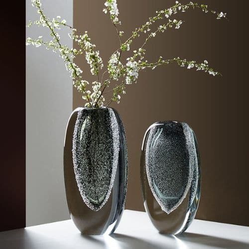 Deux vase de style Murano en verre épais à double paroi. Le cœur du vase est teinté en gris et finement bullé. Il y a un petit vase et un modèle plus grand qui contient une branche de plante verte.